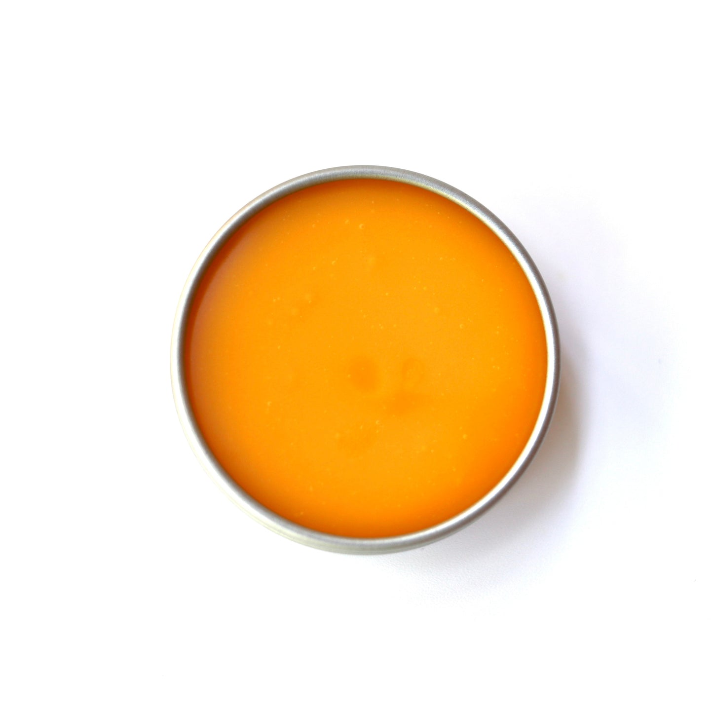 A round metal tin filled with a smooth, solid orange balm on a clean white background.