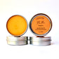 Two small round metal tins of hand salve on a white background, one showing the bright orange balm inside and the other showing the orange label with the brand name BeesButter Canada.