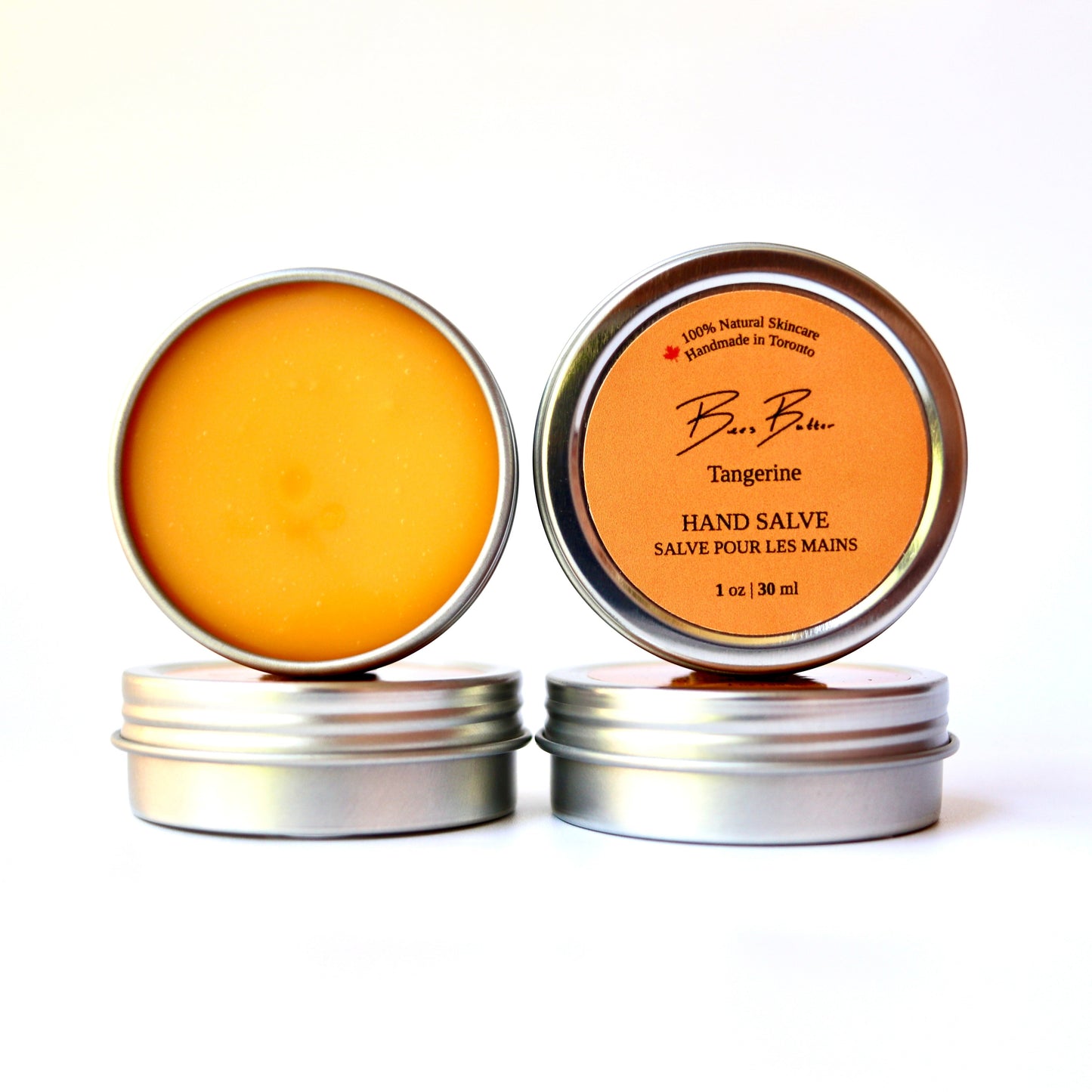 Two small round metal tins of hand salve on a white background, one showing the bright orange balm inside and the other showing the orange label with the brand name BeesButter Canada.